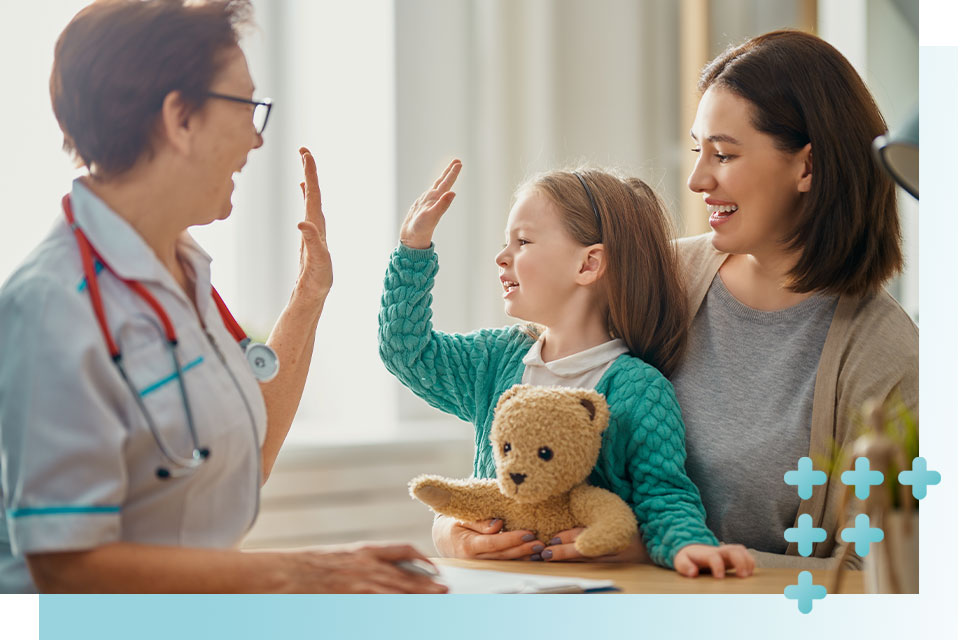 Die Ärztin sitzt gegenüber einer Frau, die ihre Tochter auf den Schoß hat. Alle drei lächeln. Die Ärztin klatscht mit der Tochter ab.